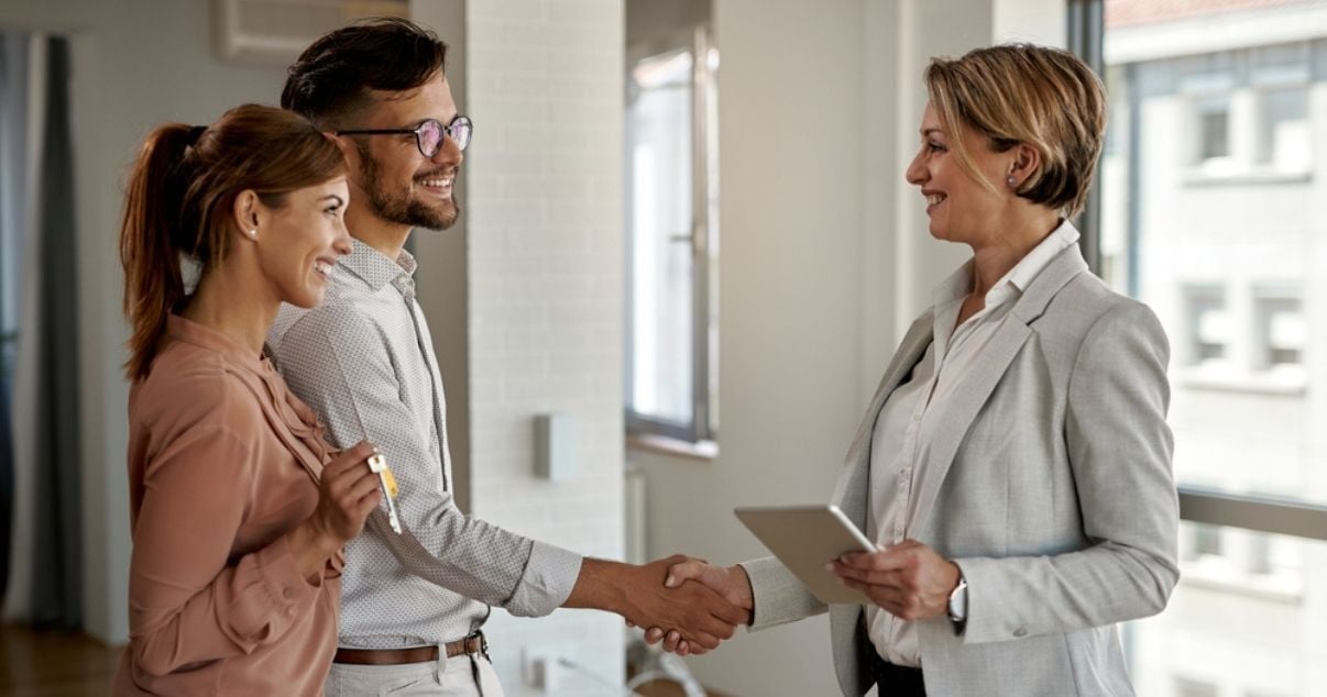 Happy young couple shaking hands with real estate businesswoman after signing a contract through smart forms